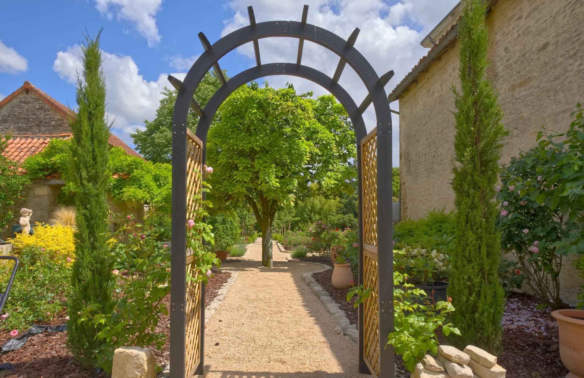 Château Lesvescault — iron garden arch framing the gravel path into the potager