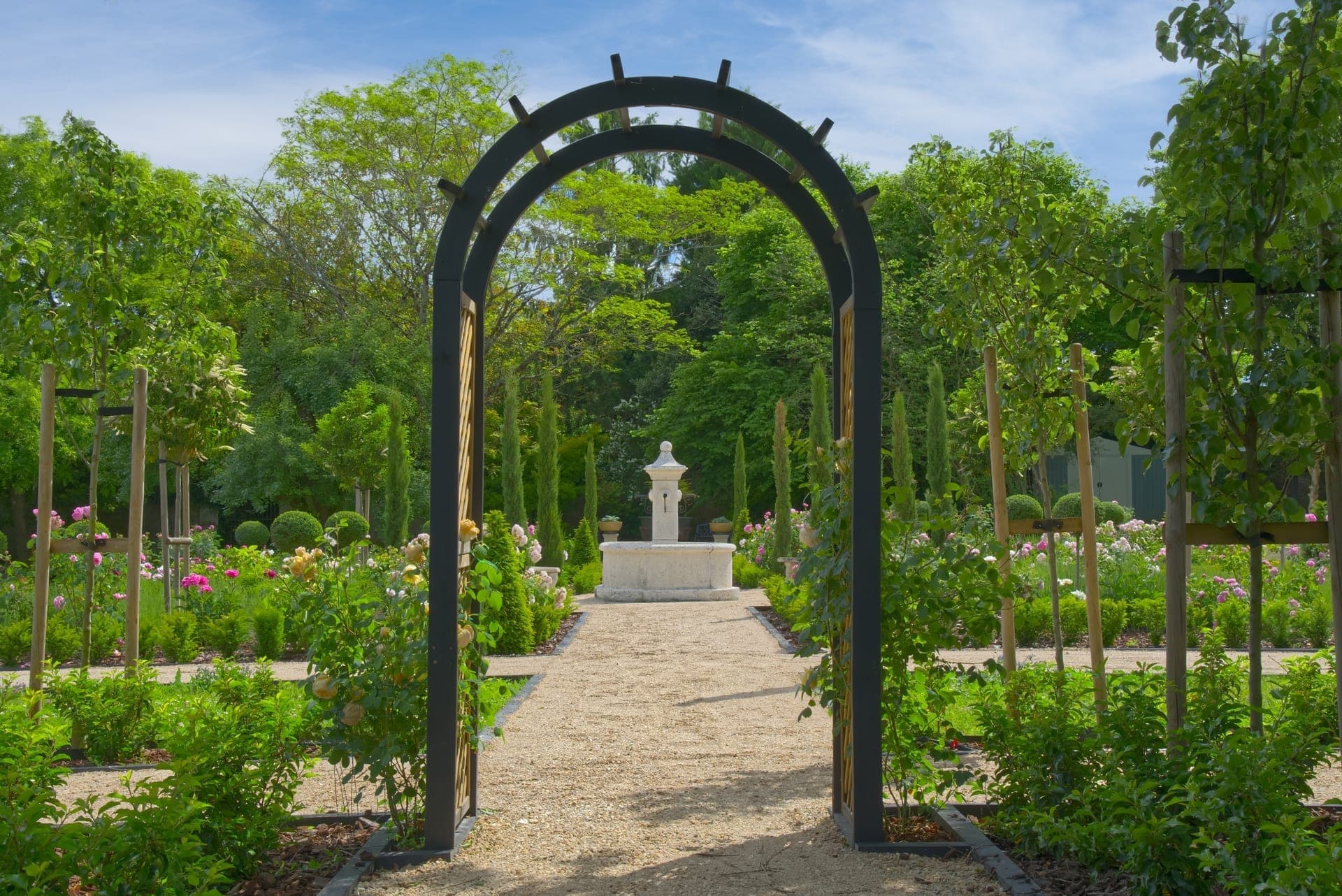 Château Lesvescault — garden arch framing the rose parterres and stone fountain beyond