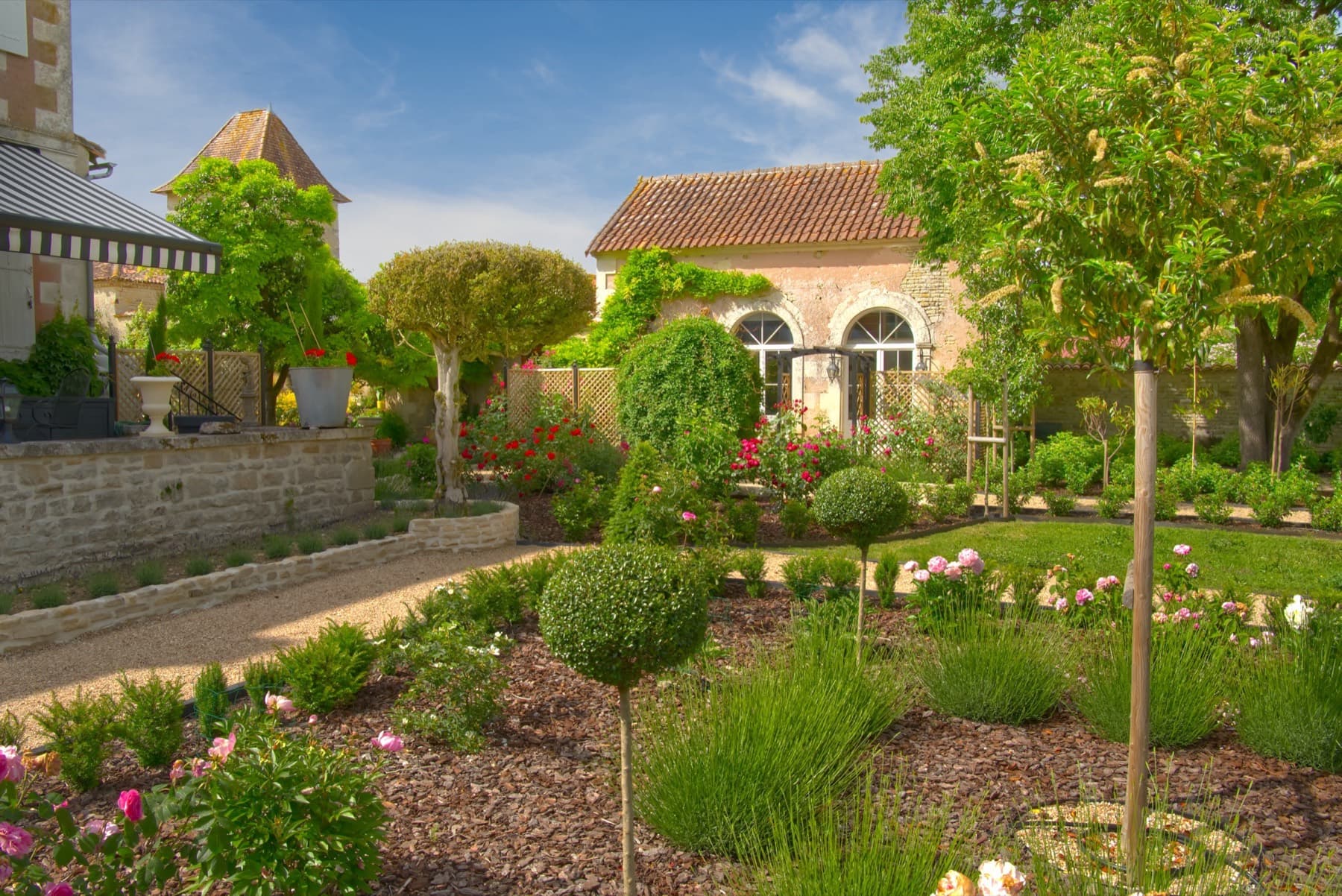 L'Orangerie — stone exterior with arched windows amid rose gardens and mature trees, Château Lesvescault