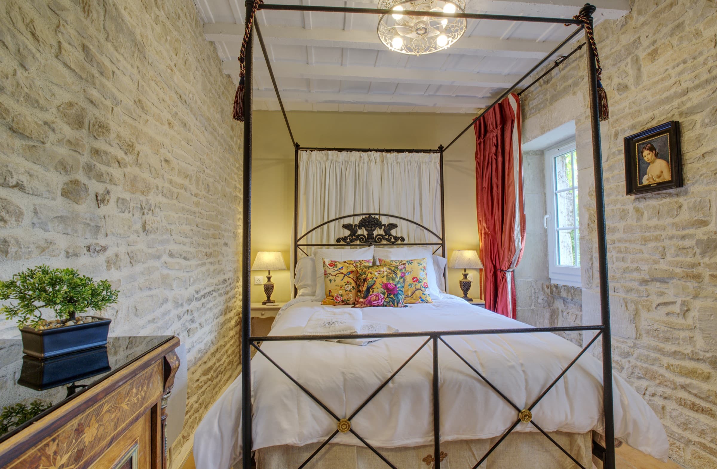 Maison Olivier — ornate iron four-poster bed with floral cushions and red silk curtains, Château Lesvescault